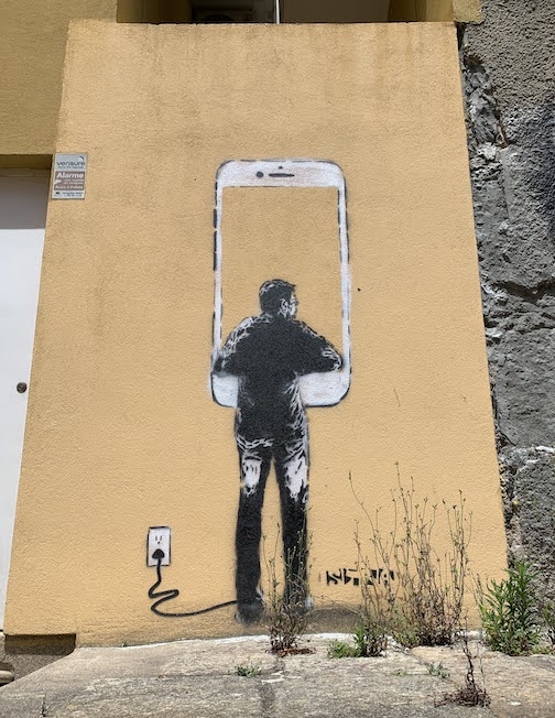 Street art - a painting of a man looking through a large iPhone.