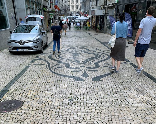 Pedestrians walk on a cobblestone design in Porto.