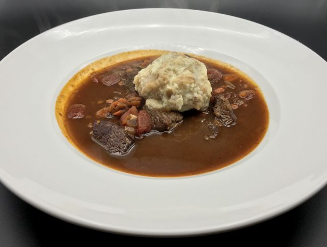 A bowl of goulash with a scallion knöedl