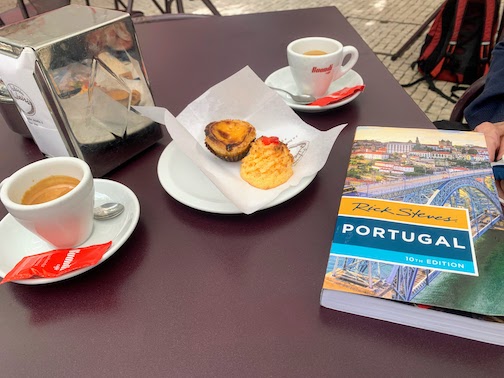 A copy of Rick Steves' Travel Guide to Portugal sitting next to some pastries and coffee at a café in Porto.