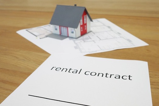 A photo showing a small model of a house, a floorplan drawing, and a rental contract document.