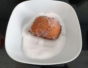 A malasada being rolled in sugar.