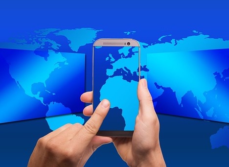 An image of hands touching a cell phone with a map of the world behind it - representing global connectivity from the phone.