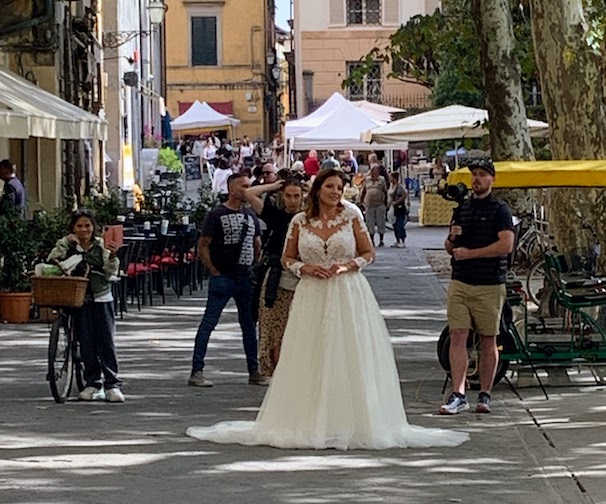 A woman in a long white bridal gown being photographed outdoors.