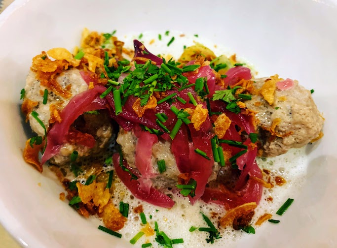 A serving of meatballs with pickled onions, red peppers, chives and other herbs.