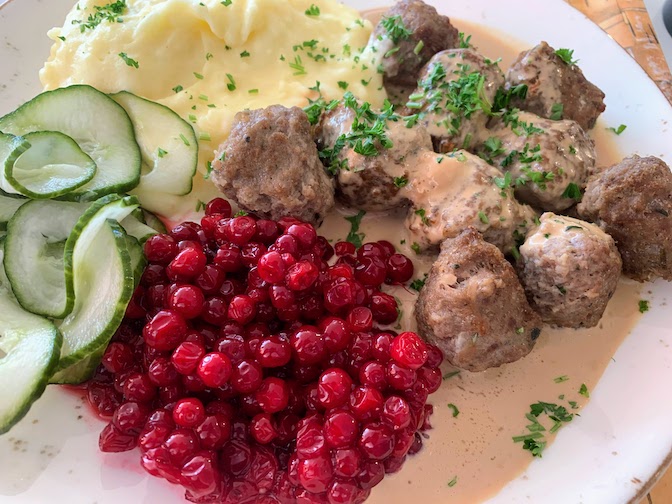 A plate of meatballs with mashed potatoes, cucumbers, and lingonberry compote.