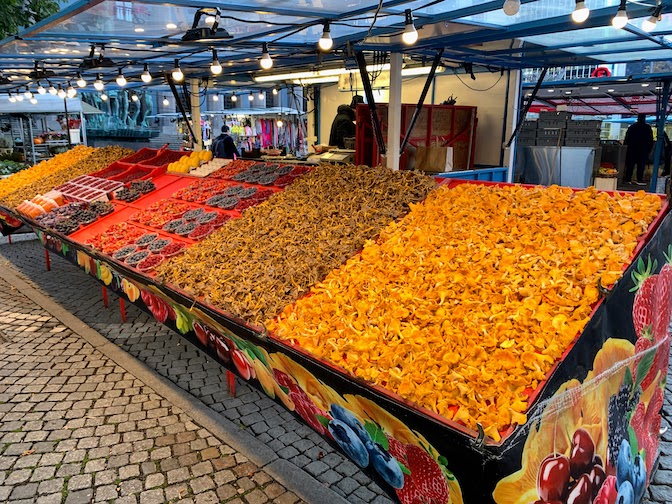 Four large displays of mushrooms along with berries for sale in an outdoor market in Stockholm.