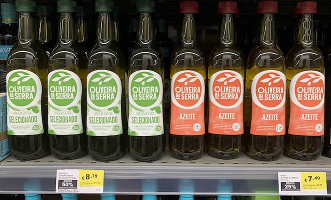 Bottles of olive oil on a grocery store shelf in Lisbon, with prices. €8.79 for extra virgin, €7.49 for regular.