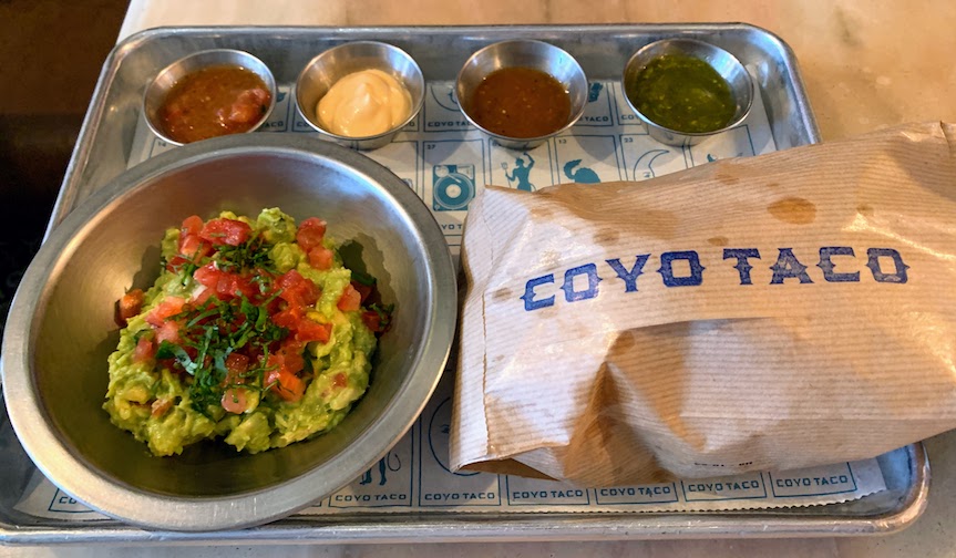 A bowl of guacamole, a bag of chips, and 4 small bowls of dipping sauce.