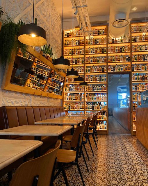 The interior of Coyo Taco, Principe Real, Lisbon, showing tables and the large liquor display rack at the rear of the restaurant.