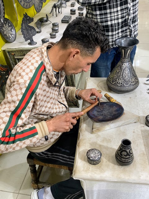 A damascene craftsman hammering thin strands of silver into a metal plate in Meknes.