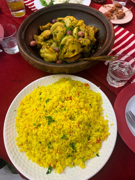 A tajine of chicken, potatoes, and olives sitting next to a plate of couscous.