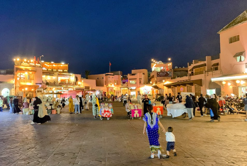 Brightly lit building surround the main square in the Marrakech medina at night.