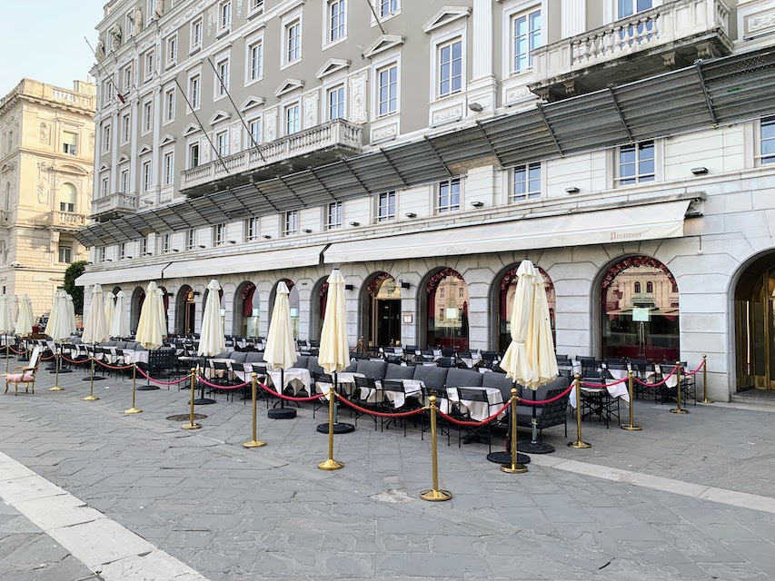 Tables, chairs, and umbrellas set out at the Caffè degli Specchi in Trieste.