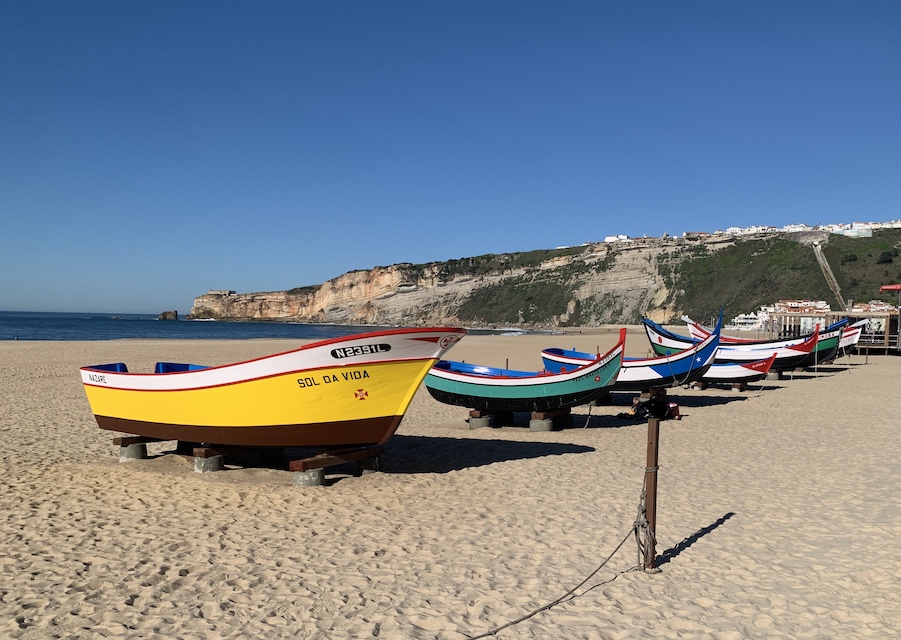 A row of colorfully painted boats under a deep blue sky on the beach at Nazaré - 16 Dec 2023