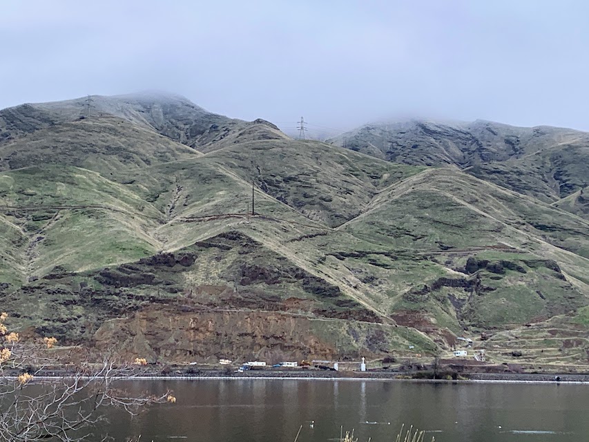 Traffic driving along the Snake River beneath the Palouse. The hillside is turning green as vegetation grows back.