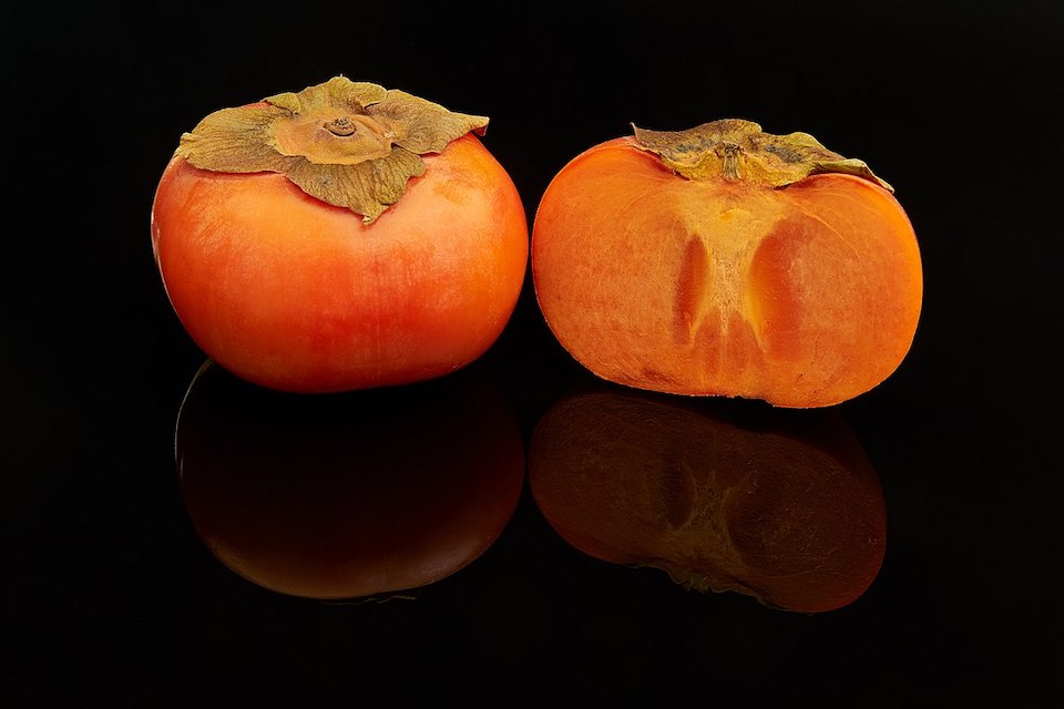 Two fuyu persimmon frutes, one cut in half.