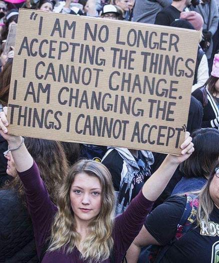 A photo of a woman protester holding a sign that says "I AM NO LONGER ACCEPTING THE THINGS I CANNOT CHANGE. I AM CHANGING THE THINGS I CANNOT ACCEPT."