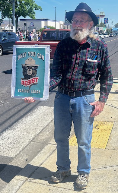 A man holds a sign saying "Only you can resist Fascist Liars", with a picture of Smokey the Bear, at the May Day rally in Clarkston, WA.