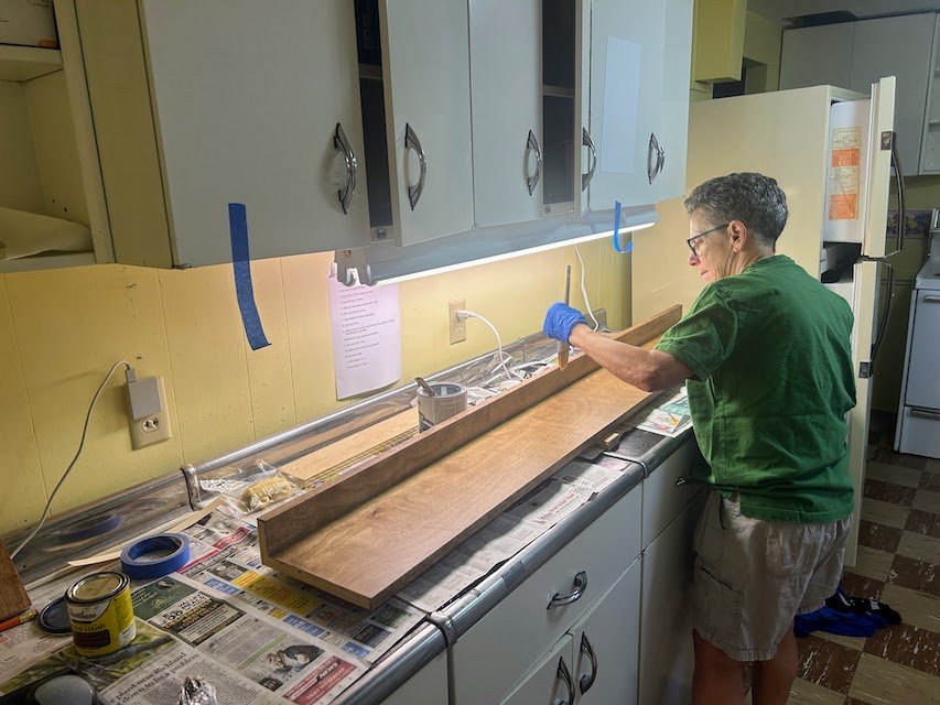Mary applying a final coat of polyurethane to one of the bottom shelves.