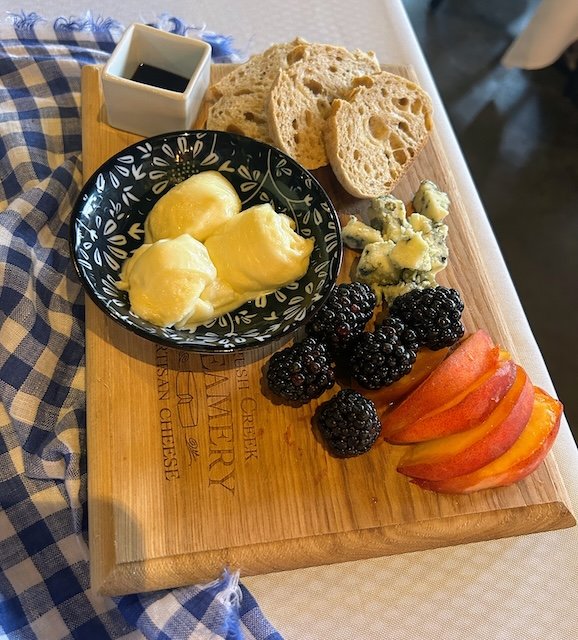 The starter - a Brush Creek Creamery appetizer board with three slices of sourdough bread, three rounds of mozzarella, small cubes of bleu cheese, some blackberries, peach slices, and a small dish of balsamic vinegar.