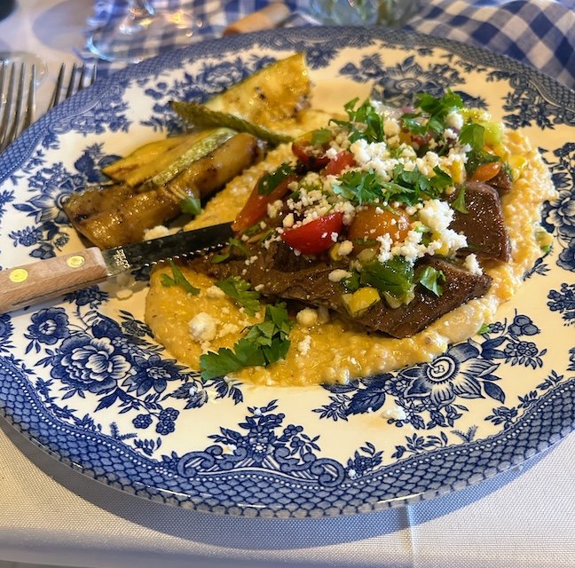 An entree - grilled flank steak with fresh smoky salsa and cojita cheese, served with green chili cheese grits and grilled local squash.